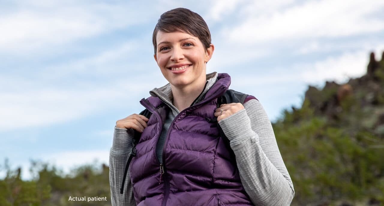 Real VWD patient Leslie holding her backpack straps and smiling.